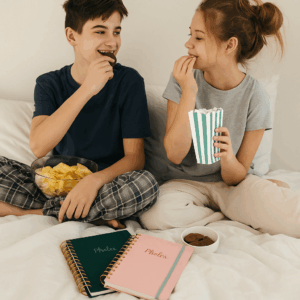 Cadeaubonnen voor brugklassers – twee tieners eten chips en popcorn met een bonnenboekje op bed.